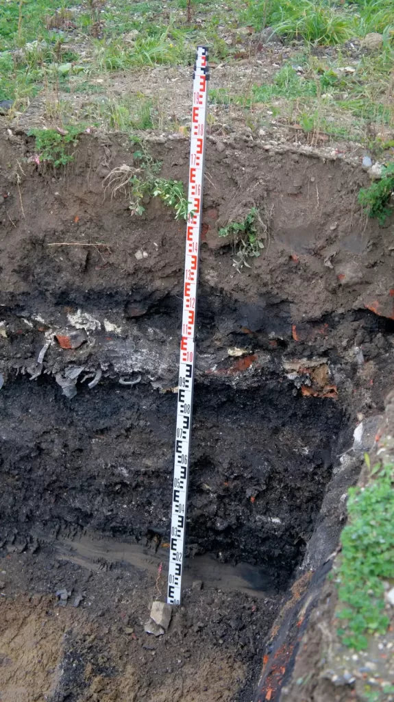 Excavated soil pit with measurement rod for soil contamination inspection – showing contaminated site assessment in progress